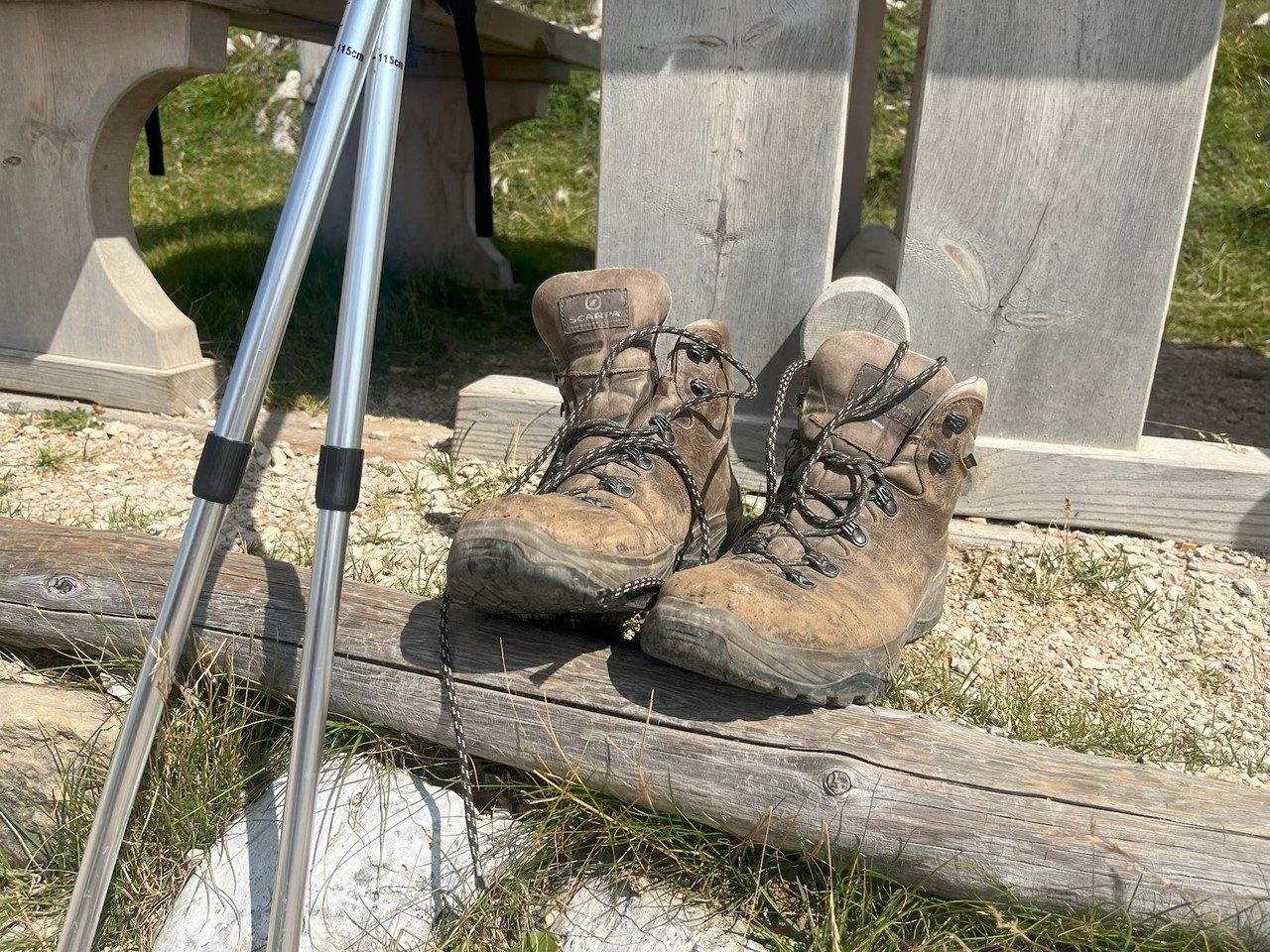 Worn hiking boots and walking poles resting against a wooden bench in the mountains