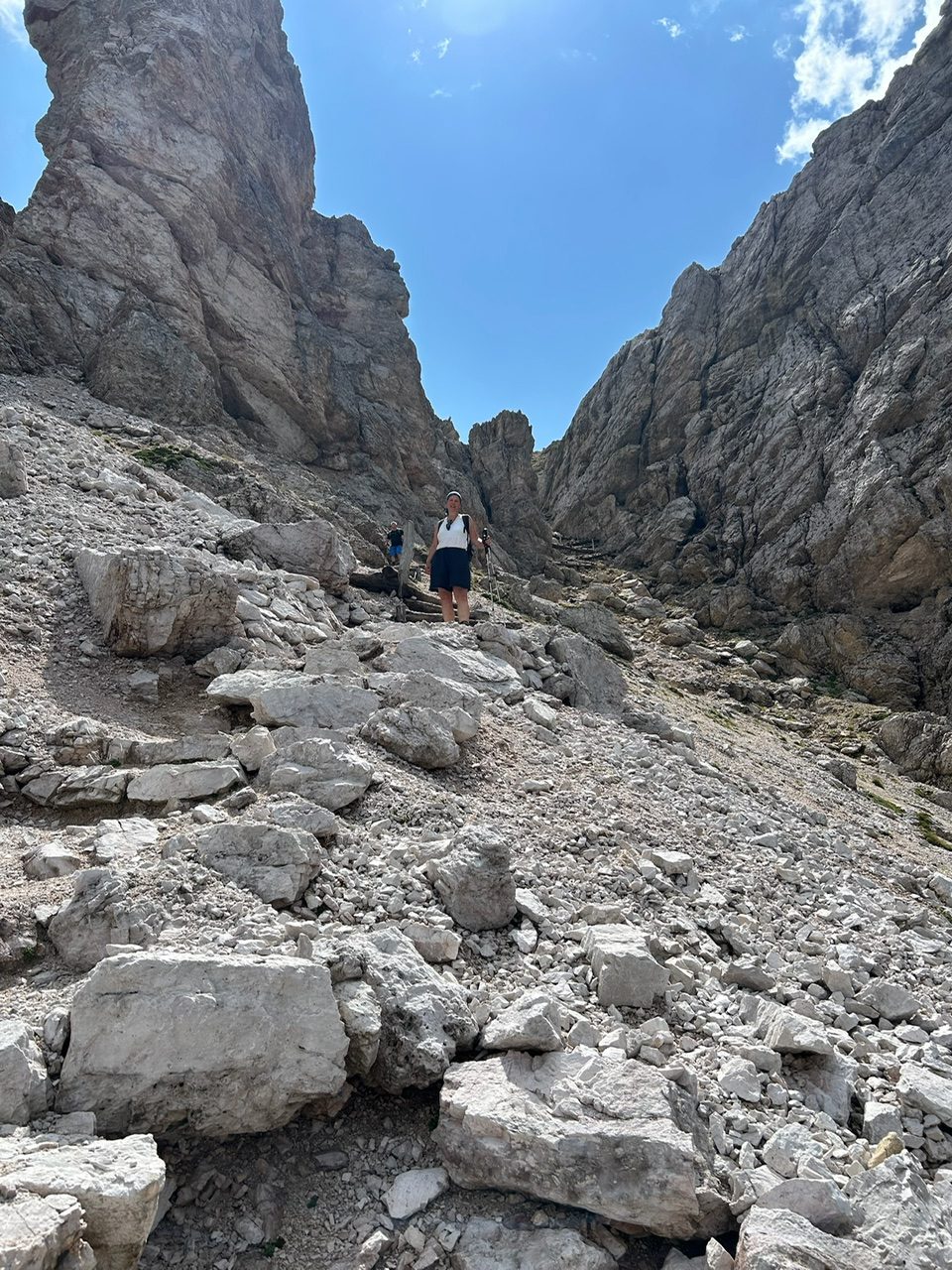 A hiker picking their way down a steep, rocky mountain path under a clear blue sky